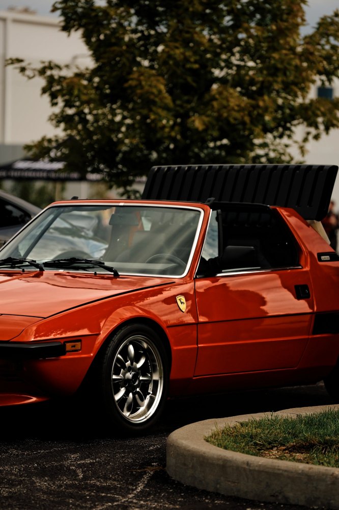 A vintage red targa parked beneath a tree, its roof panel stowed on the back
