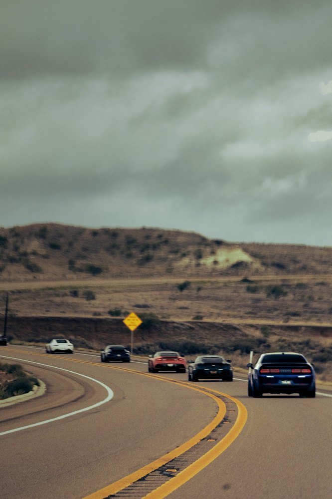 A convoy bends through a valley road under a green-grey sky