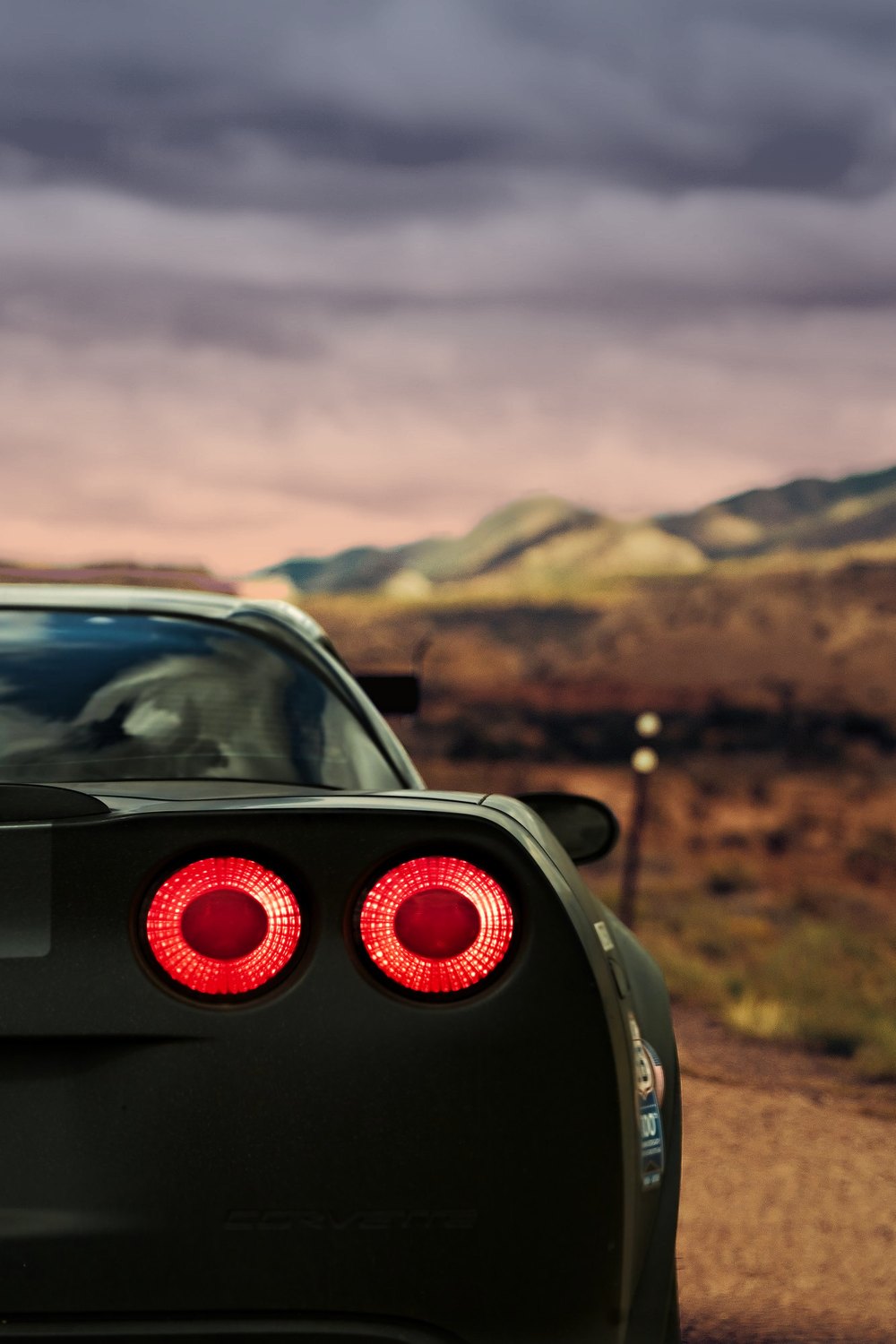 Twin round taillights of a dark Corvette glowing under a dusk sky