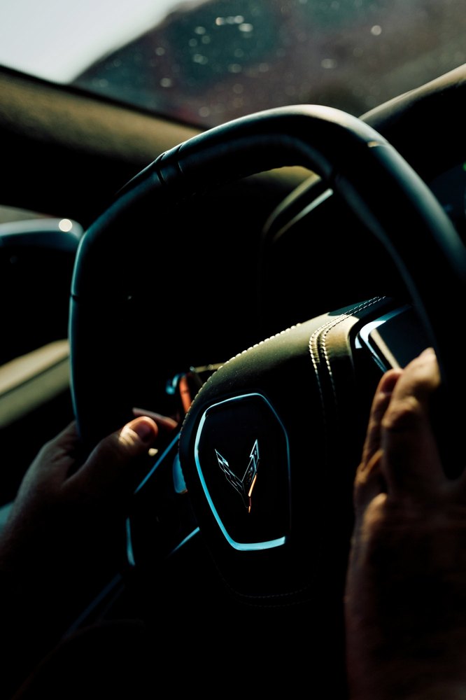 Hands on the steering wheel of a Corvette, the crossed-flags badge in low light