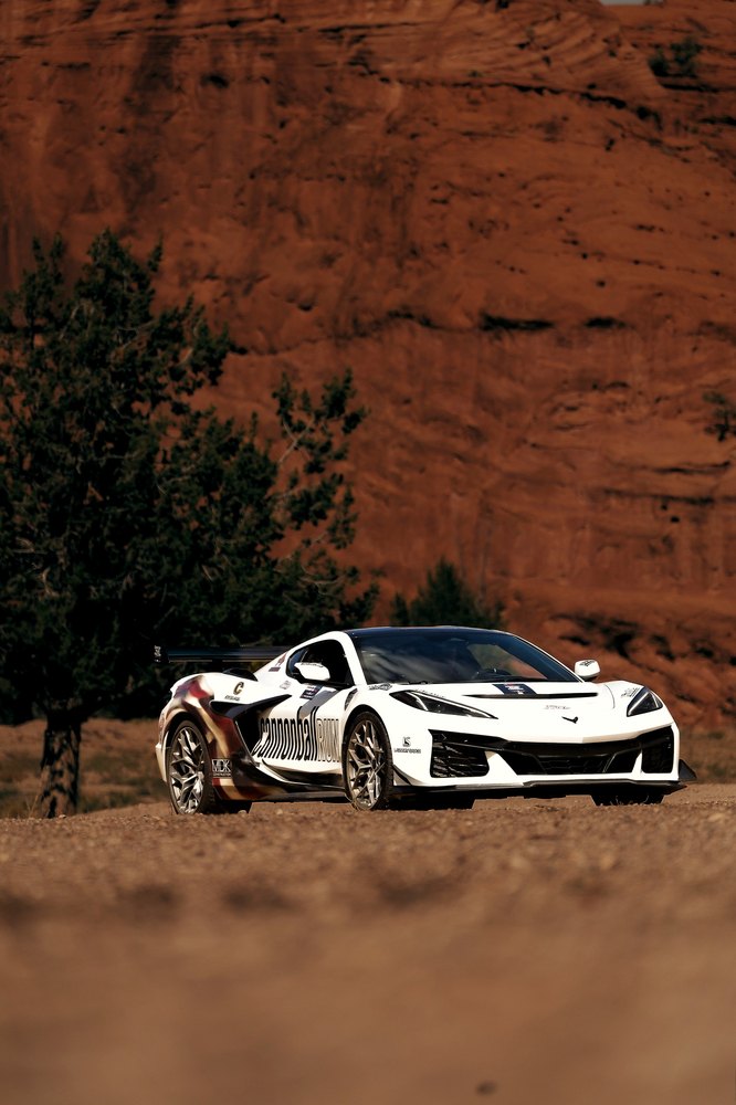 A white Cannonball Corvette low and head-on before a red sandstone cliff