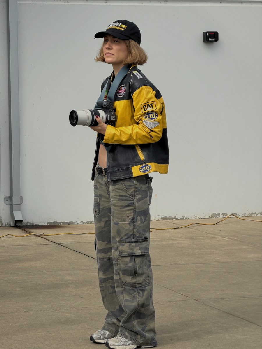Marion Vigouroux in a yellow and black race jacket, camera in hand, at a Cannonball Run stop