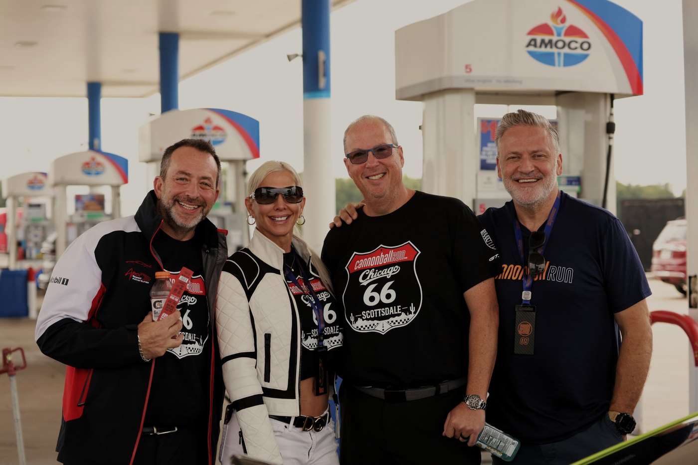 Four Cannonball drivers grin under the Amoco canopy at a fuel stop