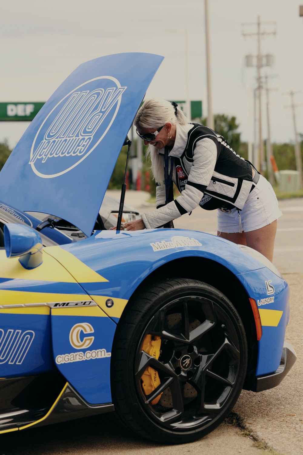 A driver checks under the raised hood of a blue liveried car at the pump