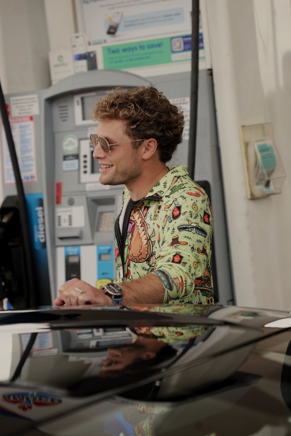 A driver in a patterned shirt waits at the pump