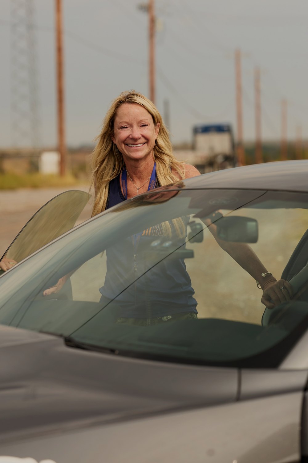 A co-driver grins over the roof of her silver car at a morning stop