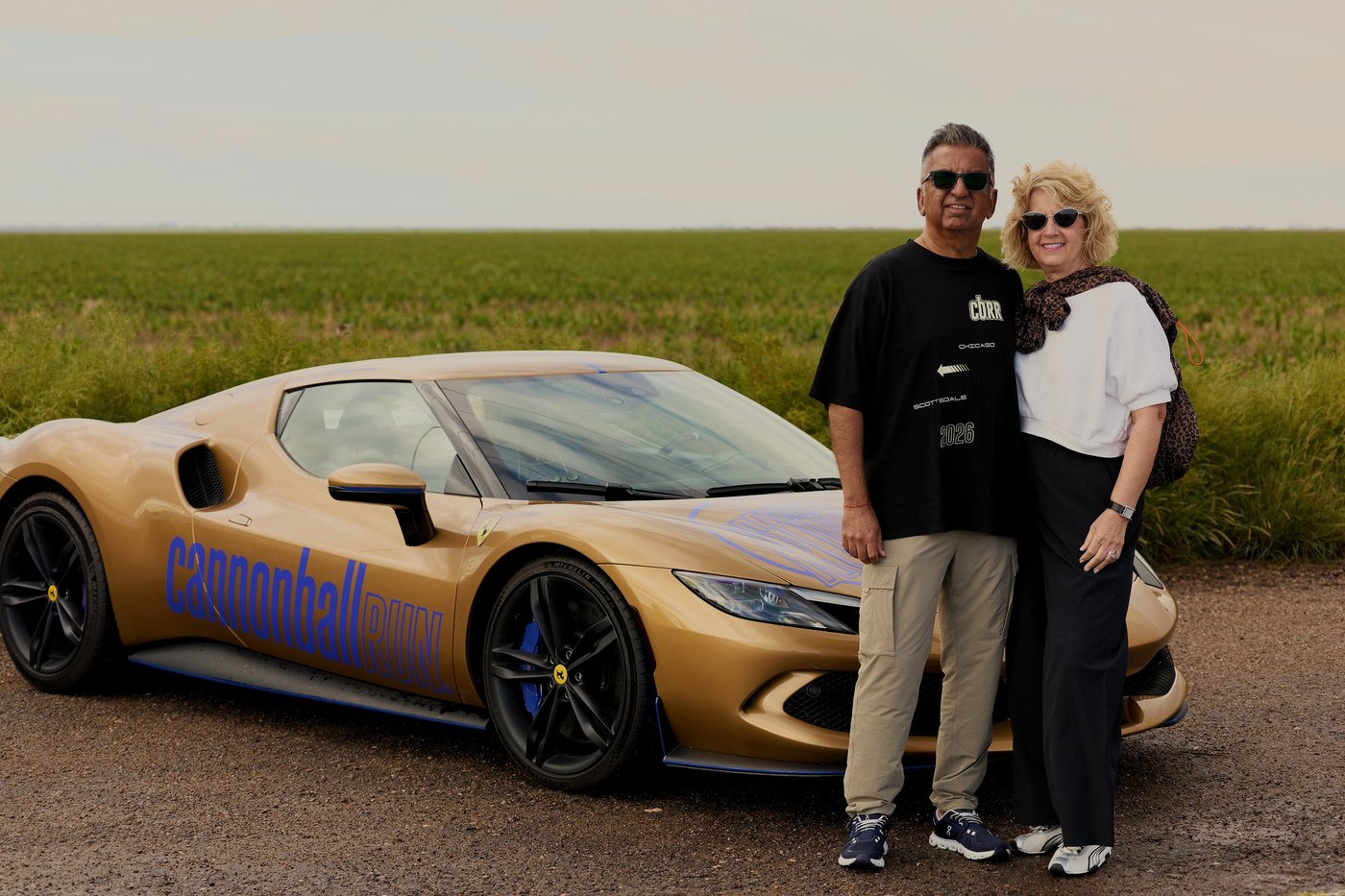 A couple beside their gold Ferrari on the open prairie