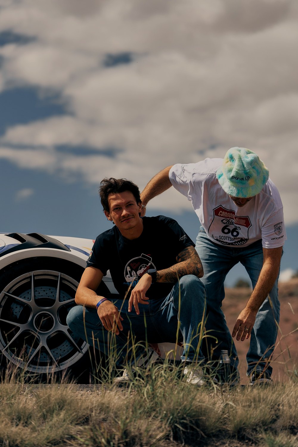 Two drivers crouch beside a liveried car on the desert verge